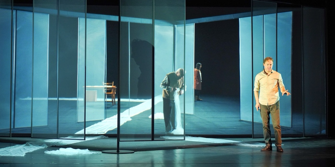 Scene from The Book of Water: an actor on stage in front of a glass pavilion