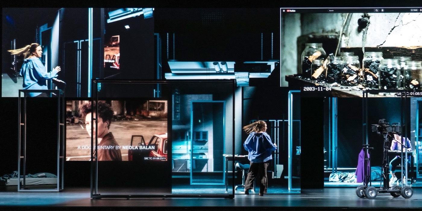 Scene from Theory of Flames: a performer on a stage of video screens and glass frames